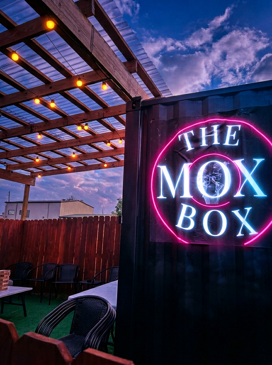 The MOXBOX outdoor patio lounge at dusk with neon signage and warm string lights